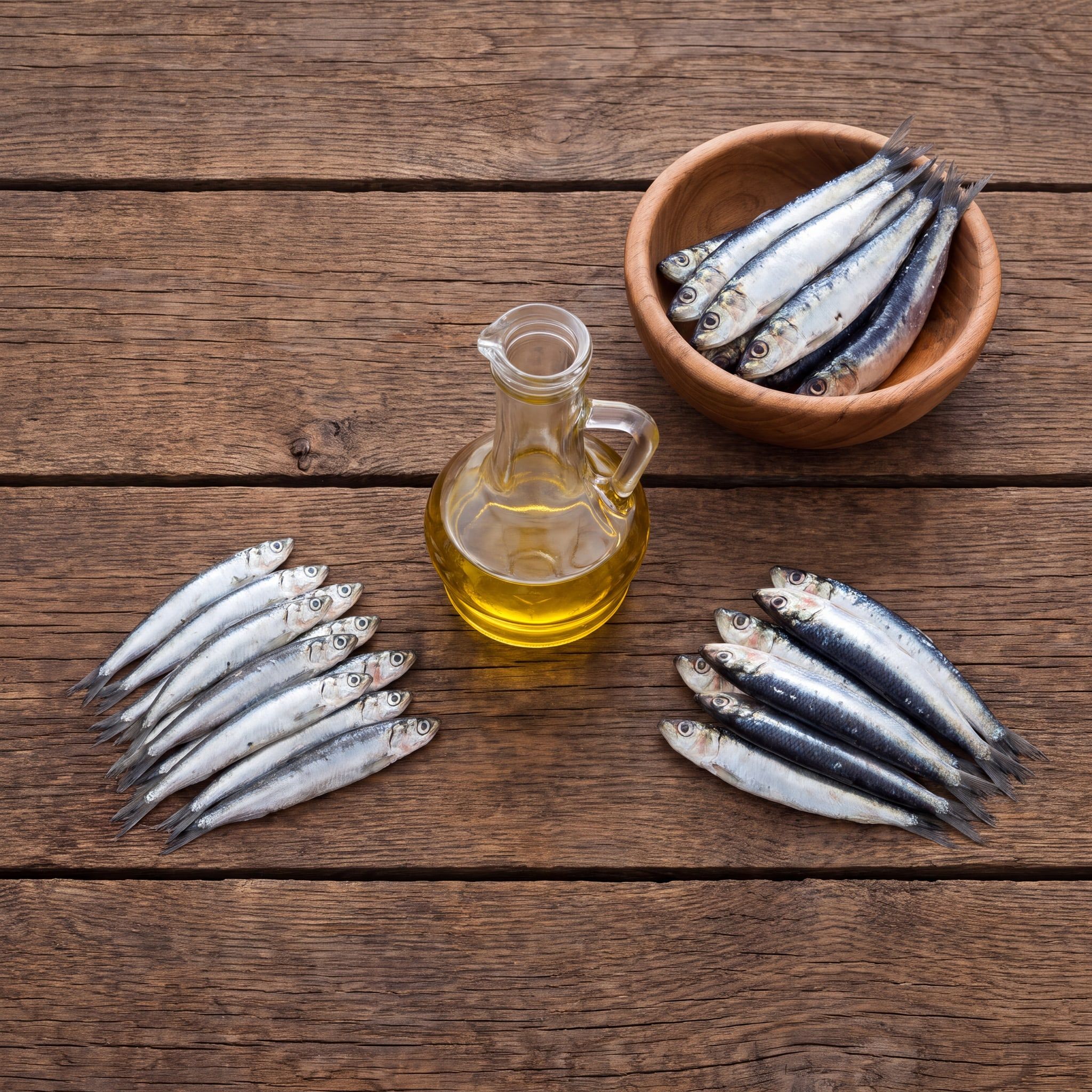 Suroviny oleje Wild Anchovy and Sardine Oil na dřevěném stole: ančovičky, sardinky a karafa rybího oleje