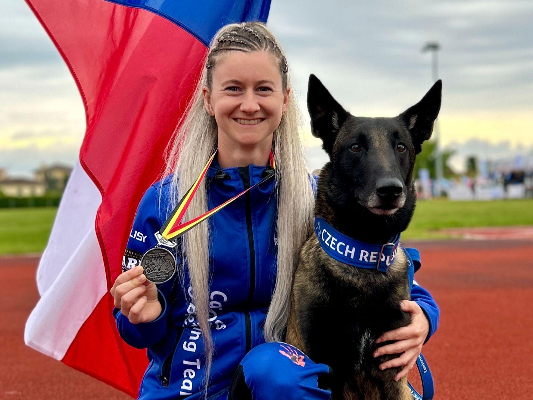Stephanie Mach s medailí a českou vlajkou, vedle ní belgický ovčák Antaios